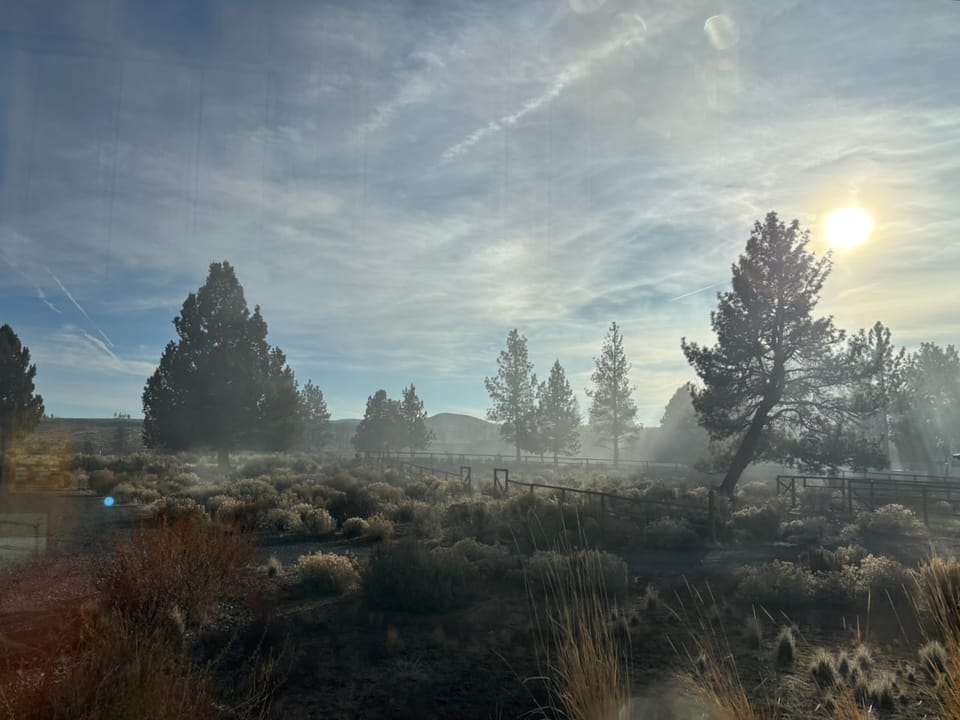 Smoke in a rural high-desert  landscape with bushes and trees.